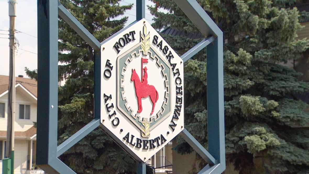 A hexagonal outdoor sign shows an emblem for the city of Fort Saskatchewan. It stands on the side of a city street.