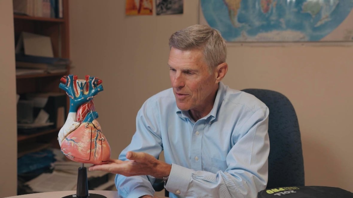 A man wearing a blue button up shirt points to a model of the heart