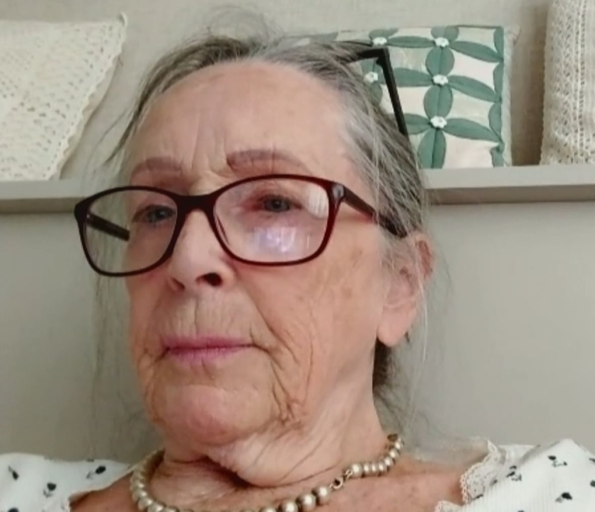 Patrick is on a zoom call, she's wearing glasses and white pearls.