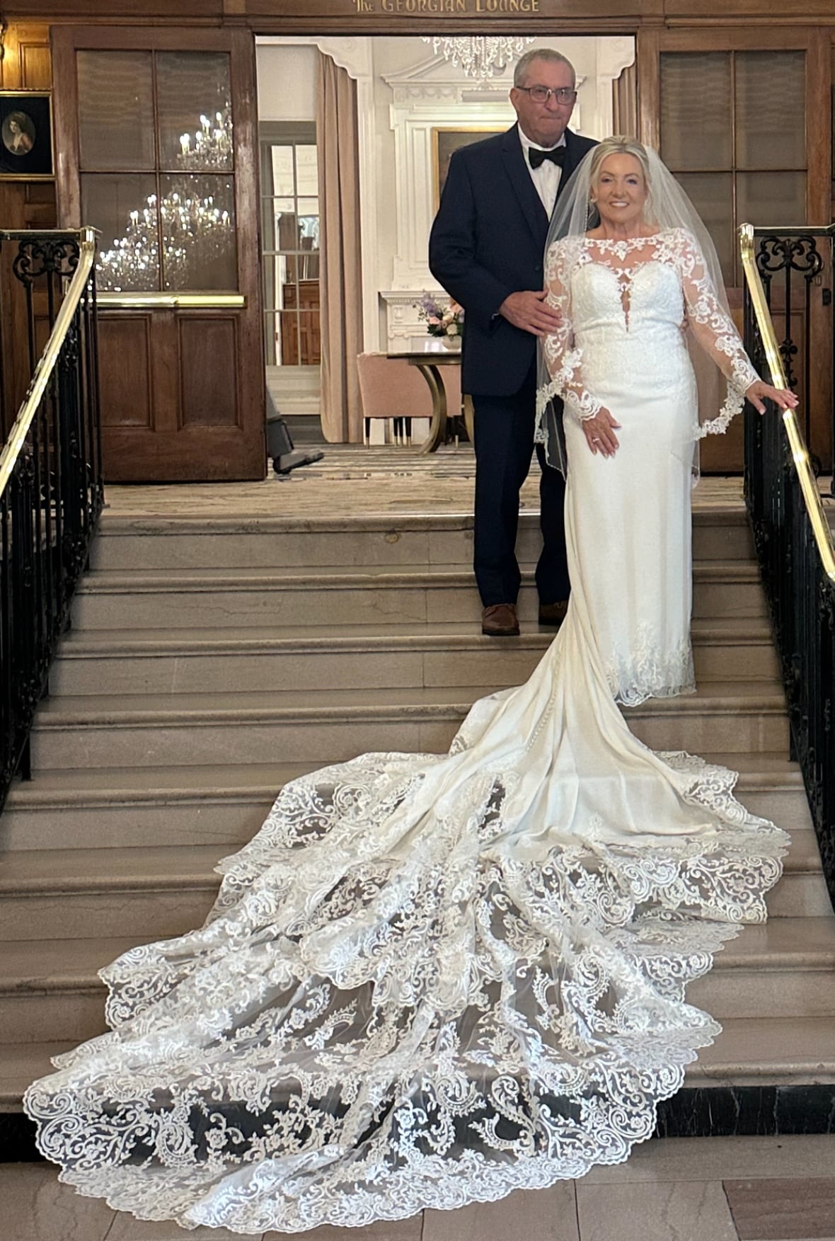 A bride and groom stand at the top of a staircase.
