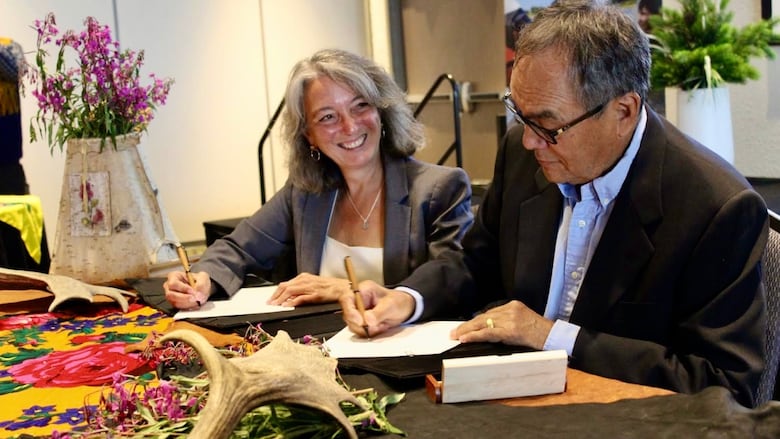 A woman and a man sign a piece of paper at a table.