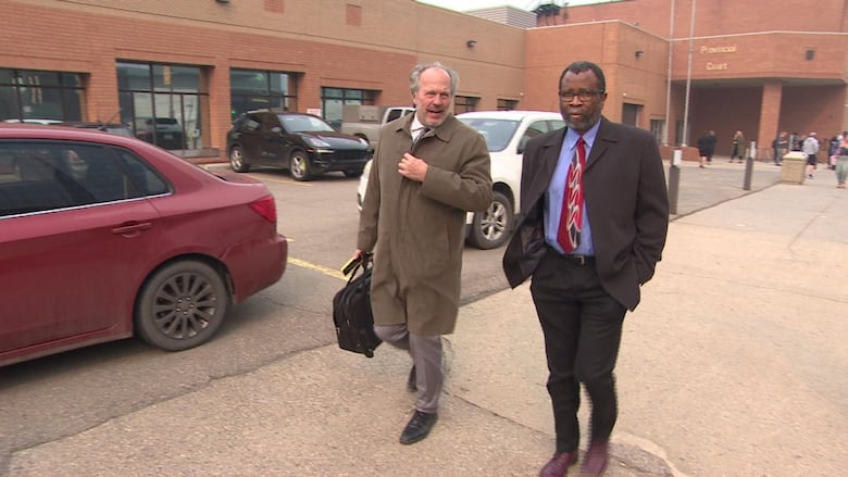 Two men in suits walk away from a prick building.