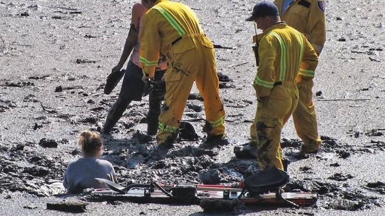Firefighters help a woman stuck in mud.