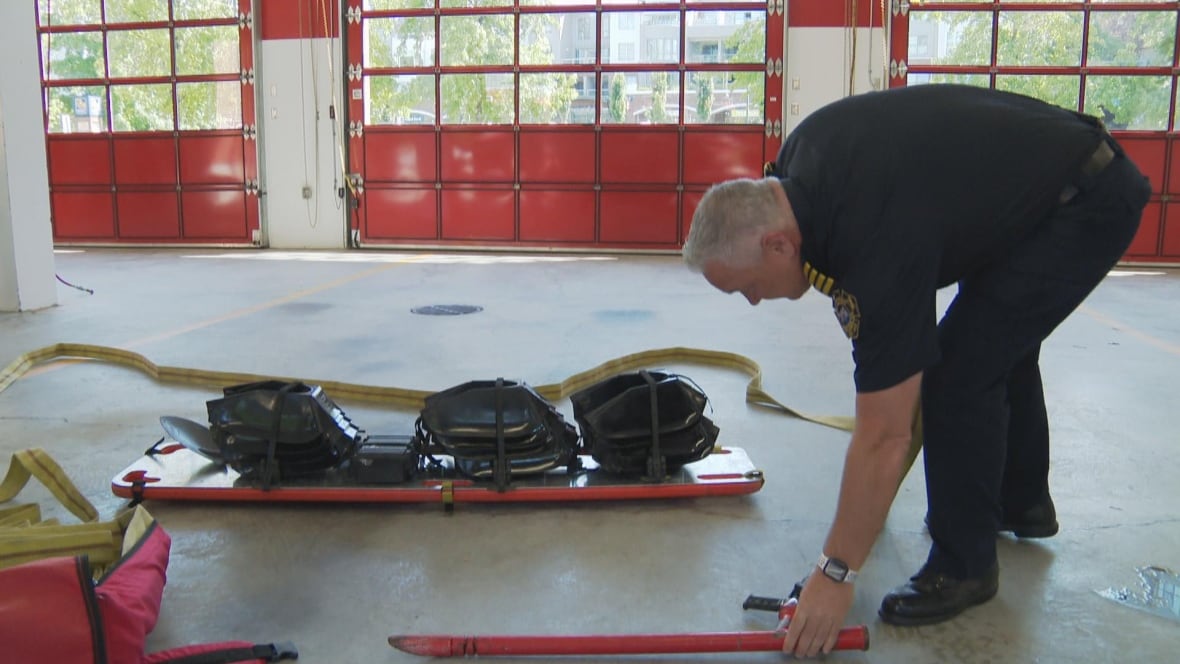 A firefighter bends to pick up a road next to a boat-like device with bags on it.