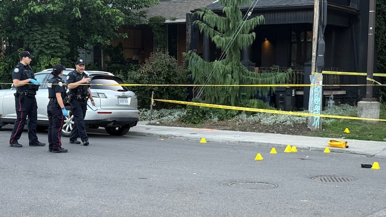 Photo showing several yellow police markers behind yellow police tape on a road. Several police offers are standing close to the markers.