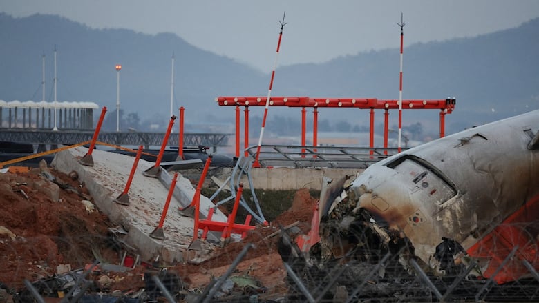 A jet plane appears to be snapped in two as it is on the ground, with significant metal and other debris.