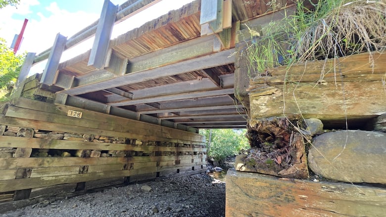 An old bridge built with cribbed railroad ties and stones sits over a dry creek bed.