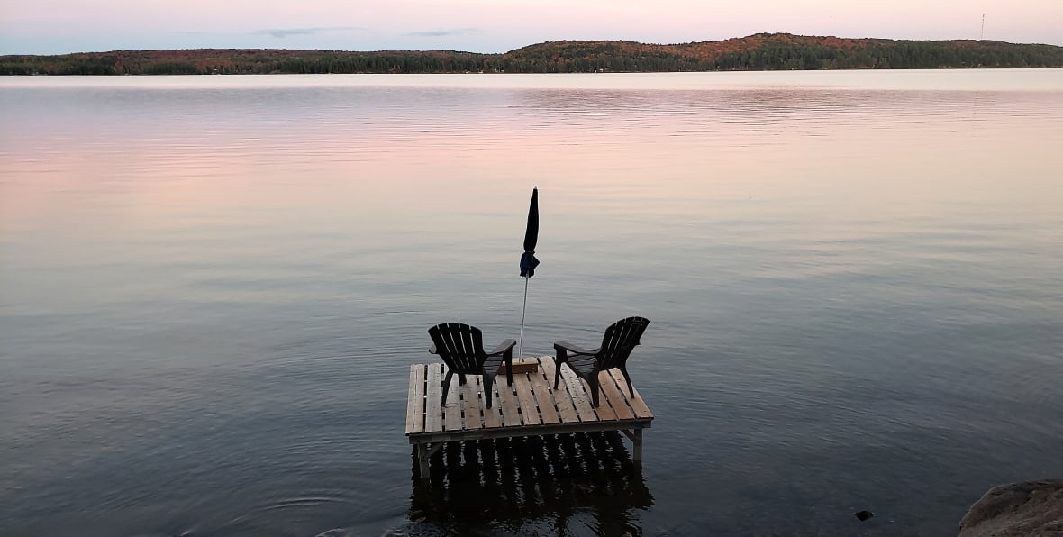 Cadeiras Muskoka ficam em uma doca com vista para um lago
