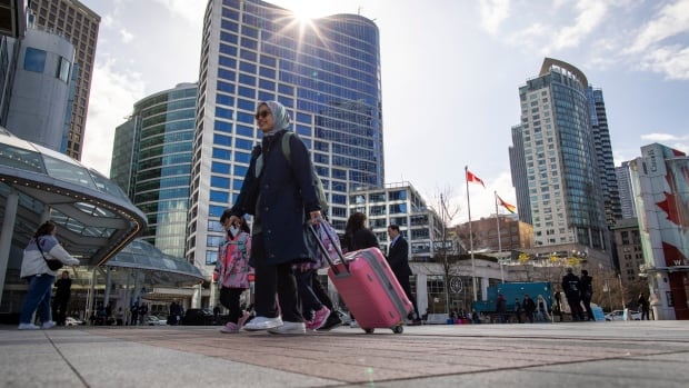 People holding suitcases walk through a downtown area
