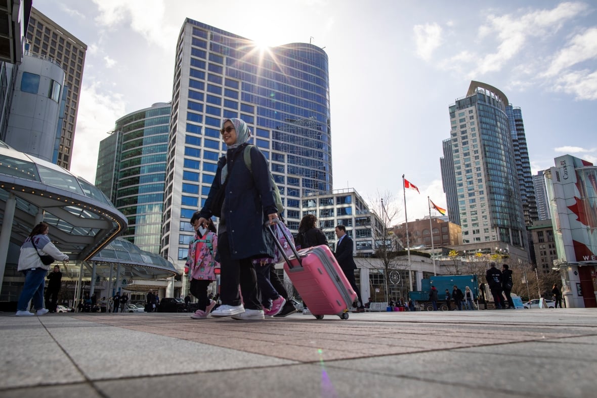 People holding suitcases walk through a downtown area