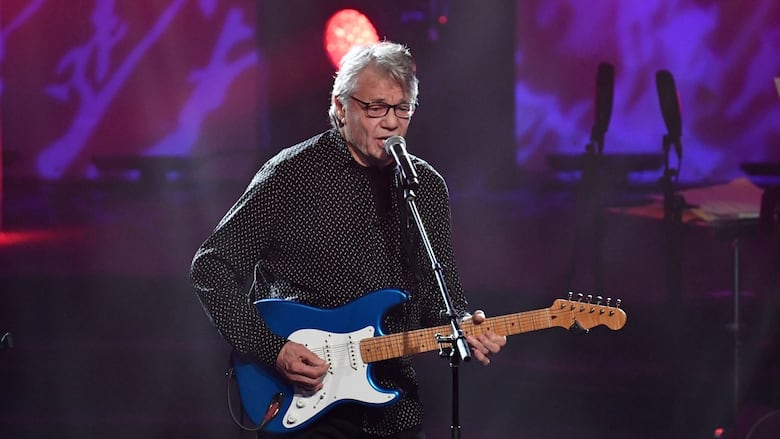 An older man plays a guitar.