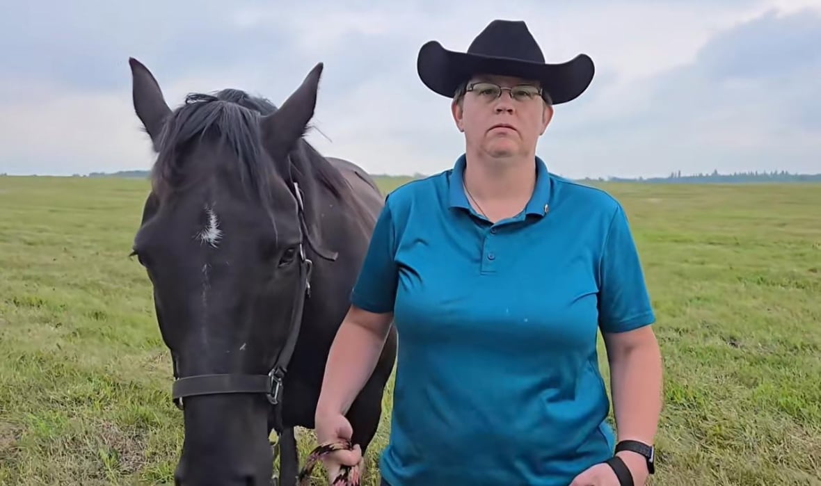 A woman wearing a cowboy hat walks a horse through a field.