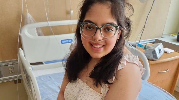 A young woman wearing oxygen sits on a hospital bed.