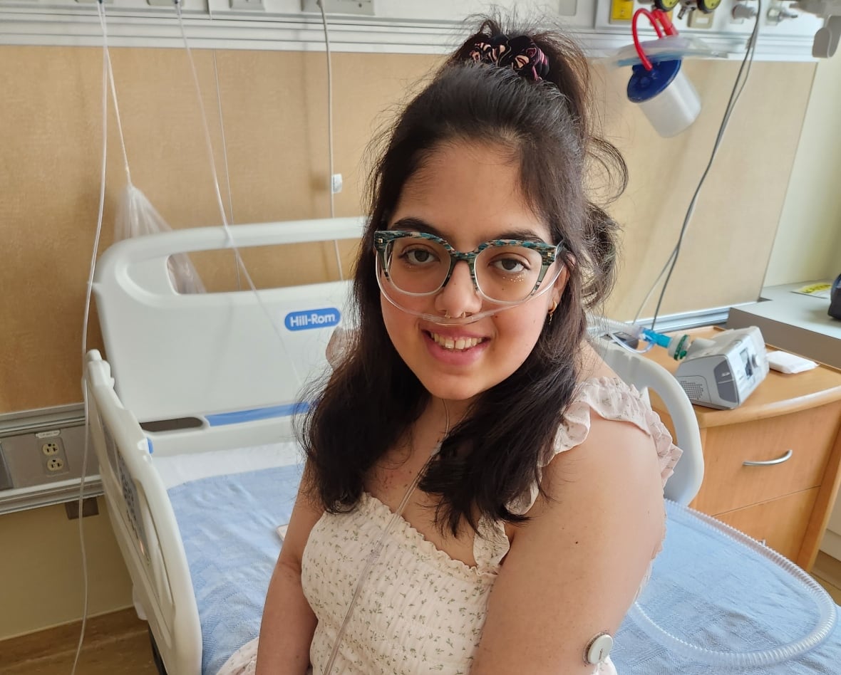 A young woman wearing oxygen sits on a hospital bed.