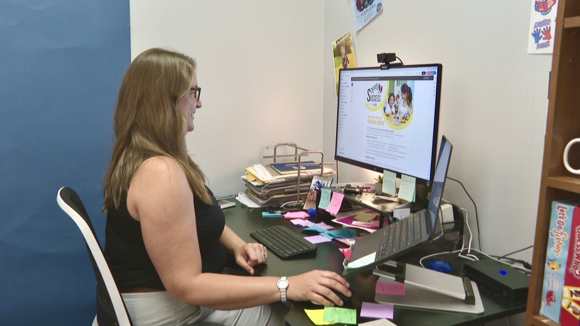 A woman with long brown hair and glasses looks at a computer screen. The screen says Steps to Success. 
