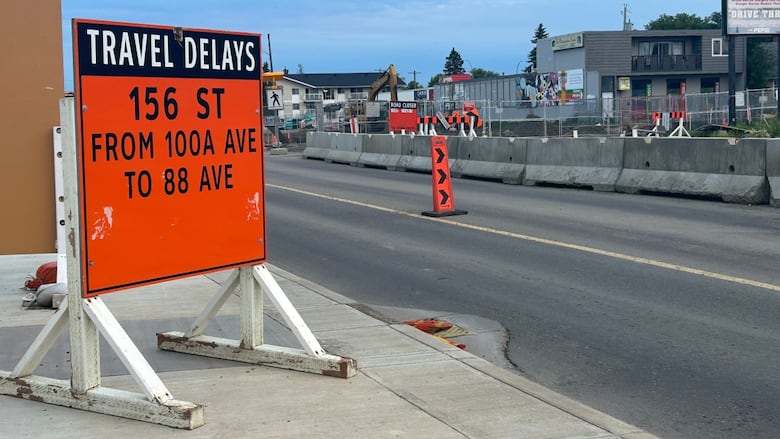 A big orange sign on the side of the road says there's travel delays on 156 street due to construction.