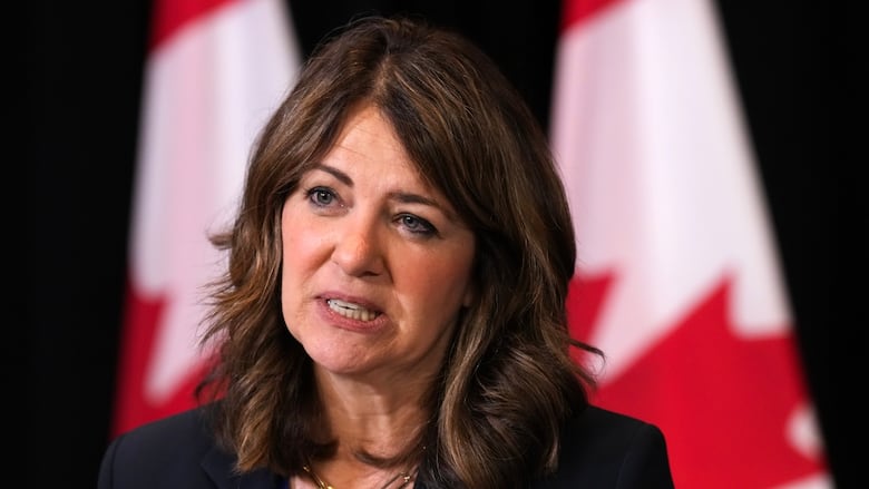 Woman nearly clenches teeth while talking. Canadian flags behind her