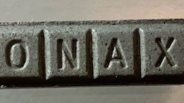 A grey rectangular pill is shown from directly above. On the side that is visible, the letters "ONAX" are imprinted.