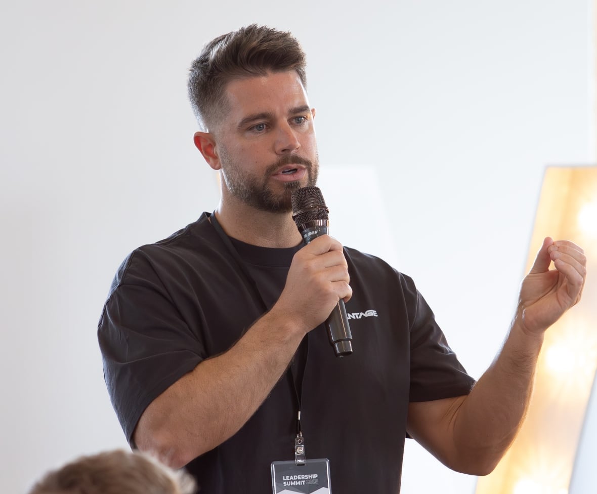 Man with black t-shirt holds microphone in front of an audience