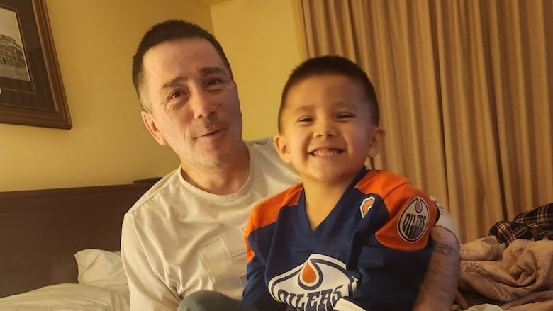Man sits with boy in arms.