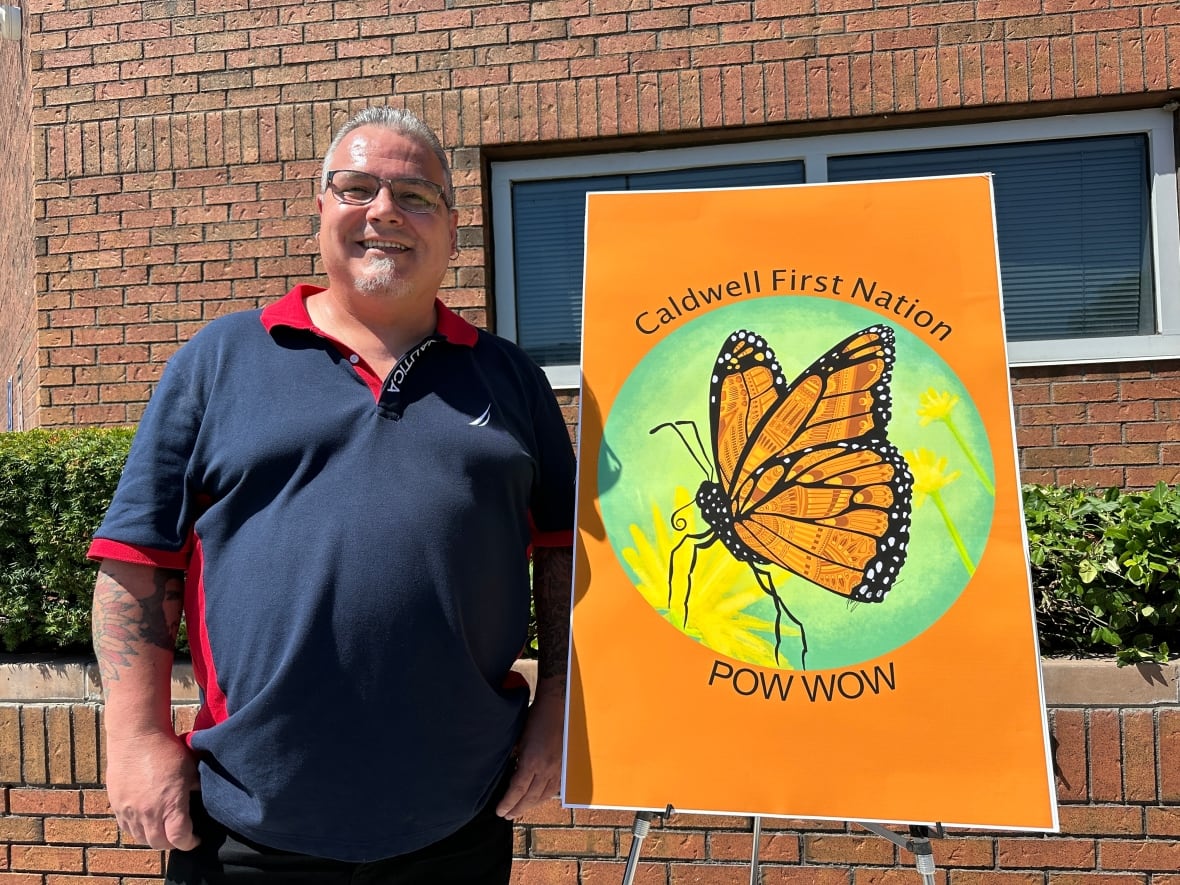 DeGraw stands with a poster on an easel for the pow wow. It has a large butterfly in the middle.