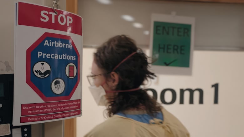 A woman wearing an N95 mask and gown passes a sign indicating to stop to take airborne precautions against the highly contagious measles virus at a hospital in Hamilton, Ont., in June 2025.