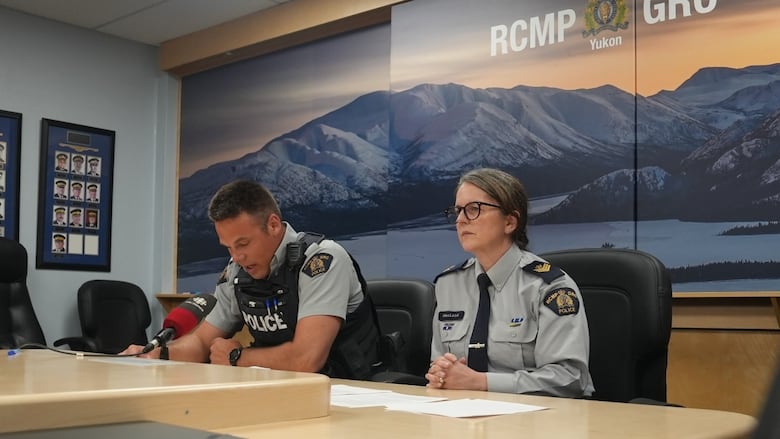 Two RCMP officers sit behind a table at microphones in front of an RCMP banner.