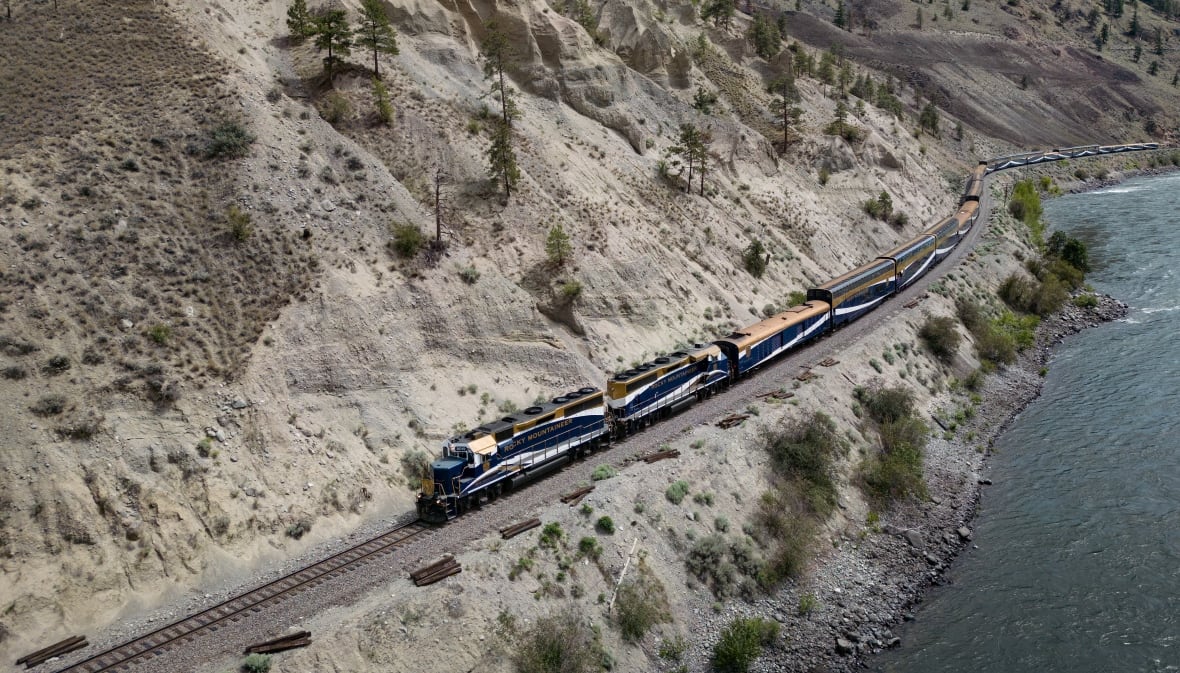 A train passes by a picturesque river valley next to a mountain.