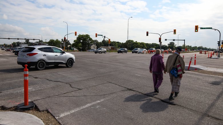 couple holds hands and walks across a wide intersection that has long, orange pylons
