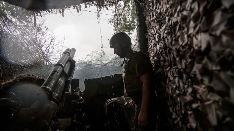 A helmeted soldier is shown in profile in a dug-out area of ground, with a large howitzer beside him.