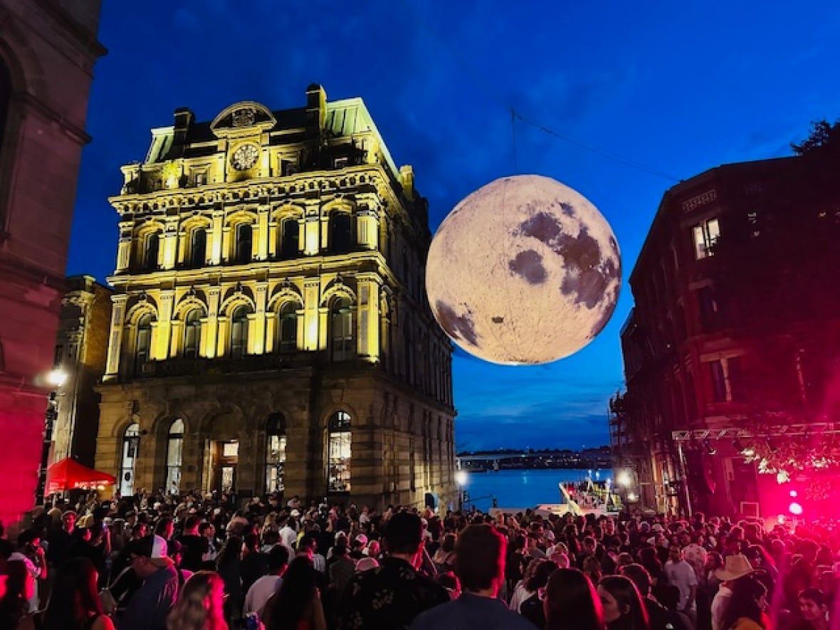 A large inflated moon hung over a crowd of people with an illuminated building next to it.