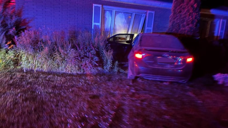 A picture of a car which has crashed into a building at night.