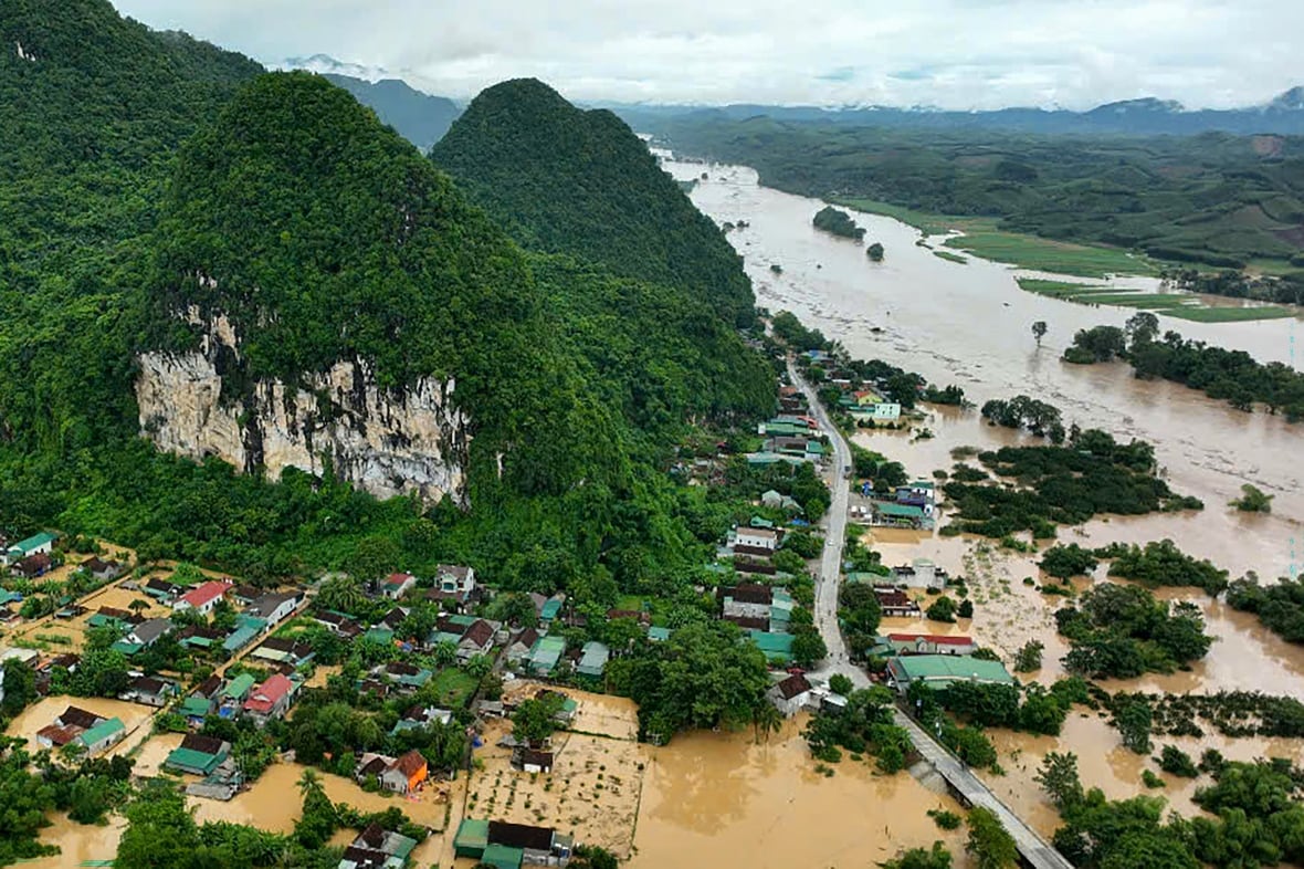 A green hill is surrounded by brown water with small buildings partially submerged.
