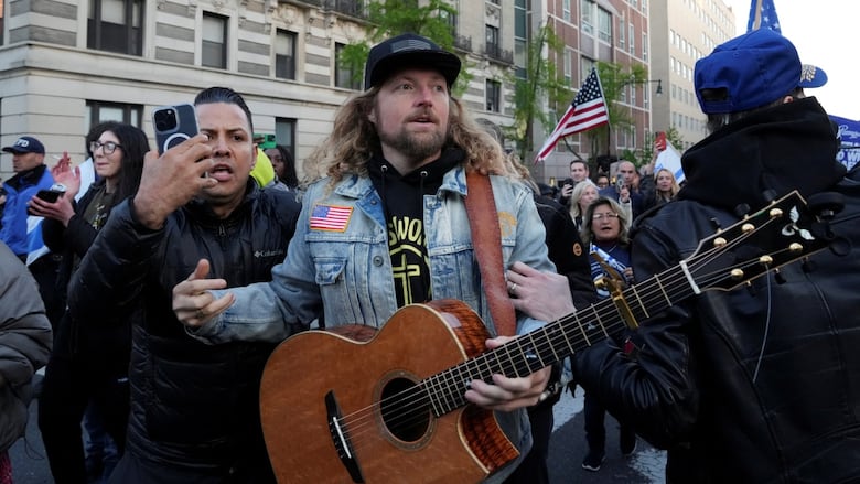 A man with long hair holds a guitar during a rally.