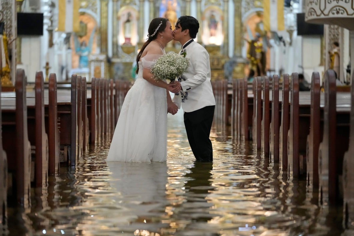 A woman in a white dress and a man wearing a suit kiss in a large stone building while standing in water.