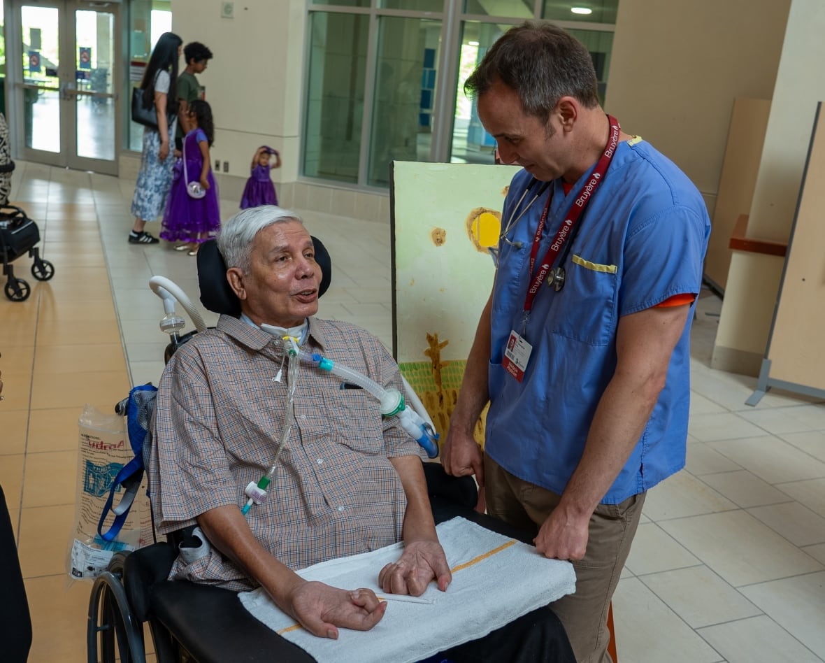 Dr. Chris Kirby talking with a patient at the Hallways of Hope exhibit, as other attendees view the artwork in the background.