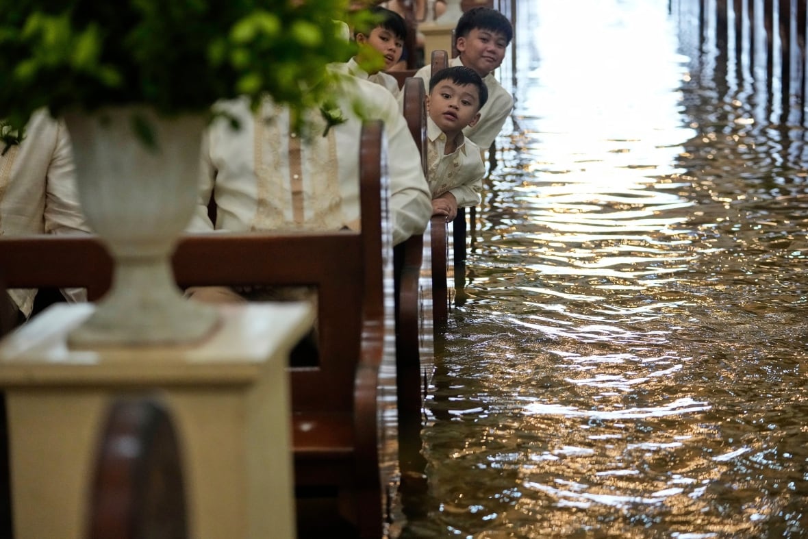 A young boy peers around a bench in a large stone building as water covers the floor.