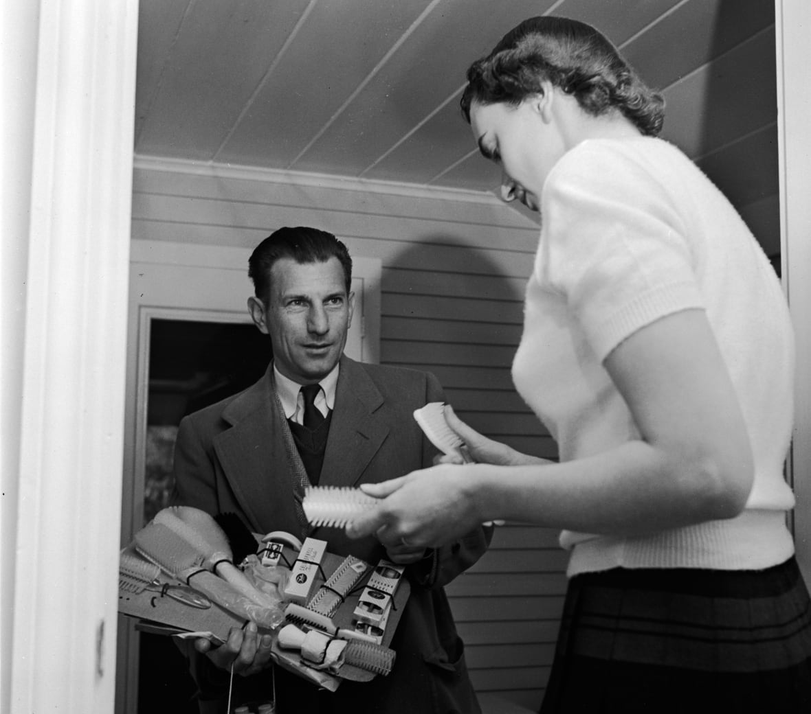 Black and white archive photo of a door to door salesman showing grooming products to a woman.