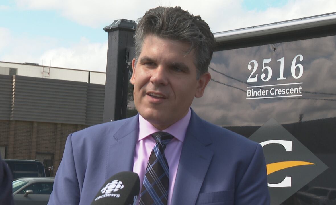 A man in a blue suit speaks into a microphone outside
