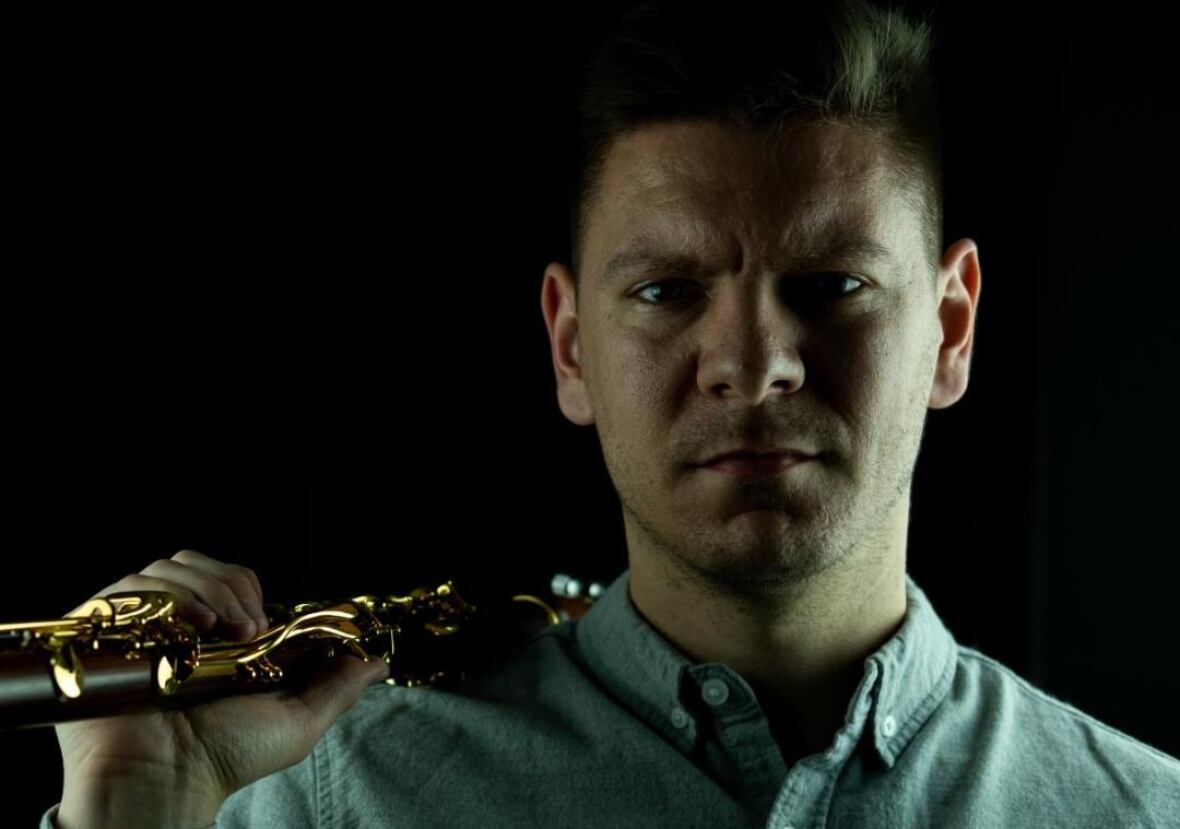 A straight-faced man holding a clarinet on his shoulder