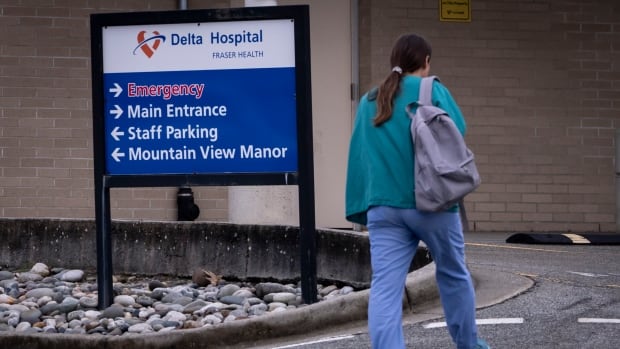 A woman walks by a sign that says Delta Hospital.