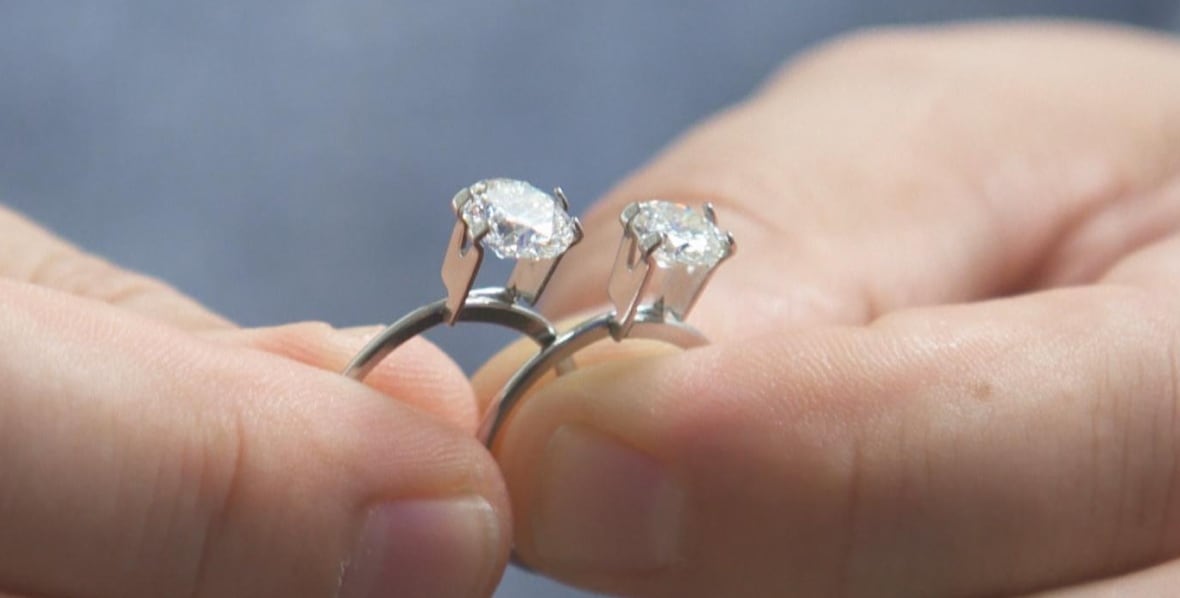 Dois diamantes nos anéis são exibidos de perto, mantidos nas duas mãos de uma pessoa.
