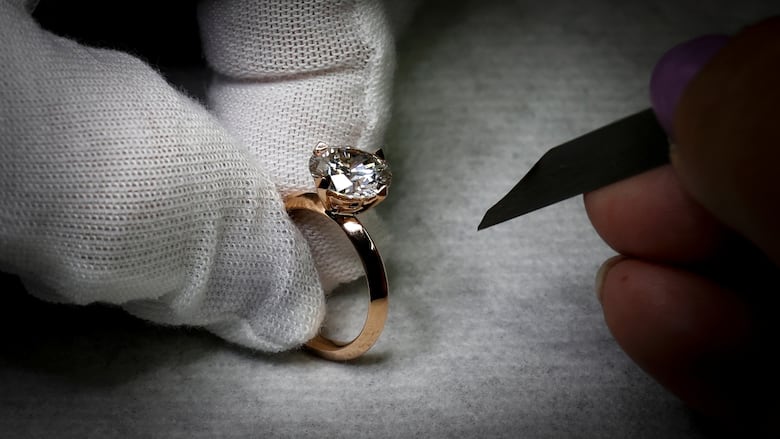 a white gloved hand holds a diamond ring in a gold band