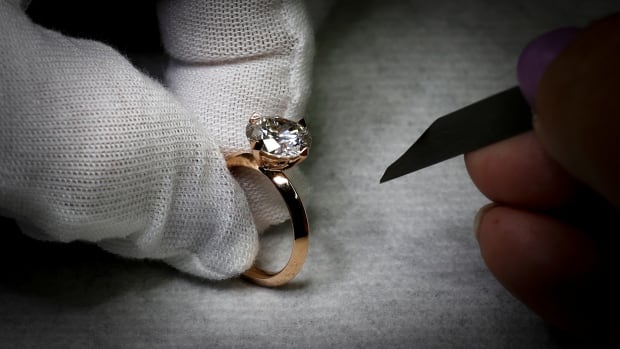 a white gloved hand holds a diamond ring in a gold band