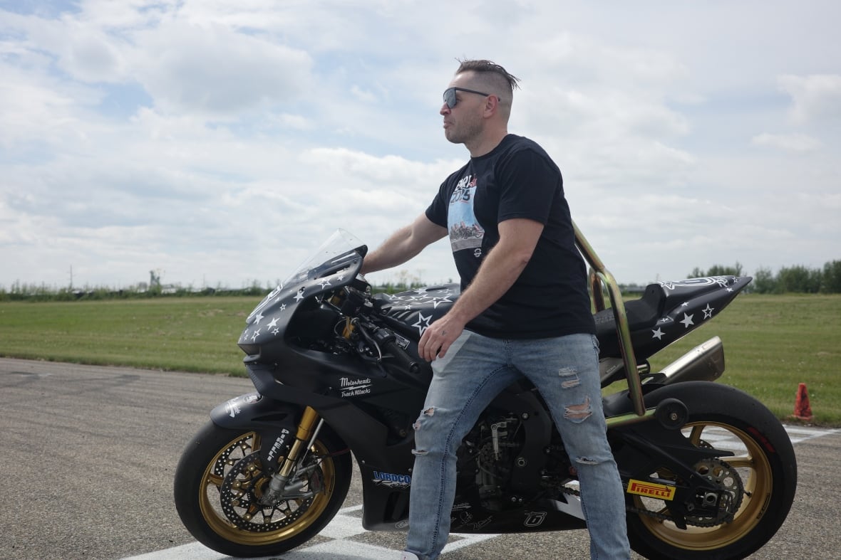 Jon Bullee faces away while standing in front of his black Honda motorcycle. 