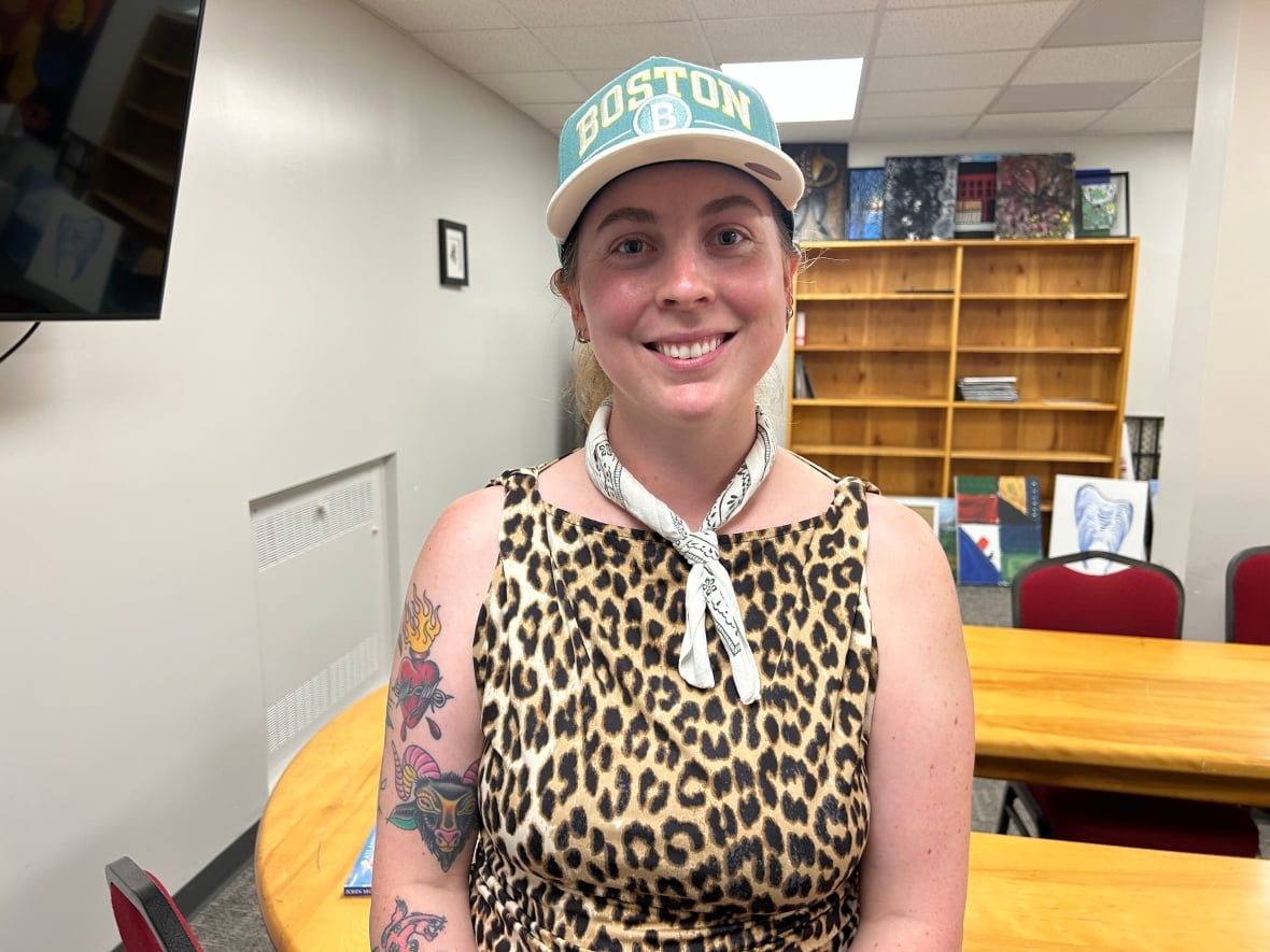 Person wearing a baseball hat and spotted shirt smiling at the camera.