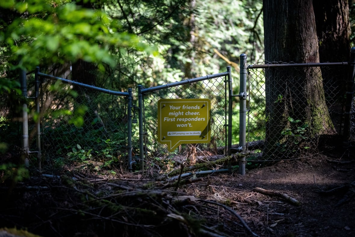 A green-yellow sign is attached to a fence in a forest. It reads, 'Your friends might cheer. First responders won't.'
