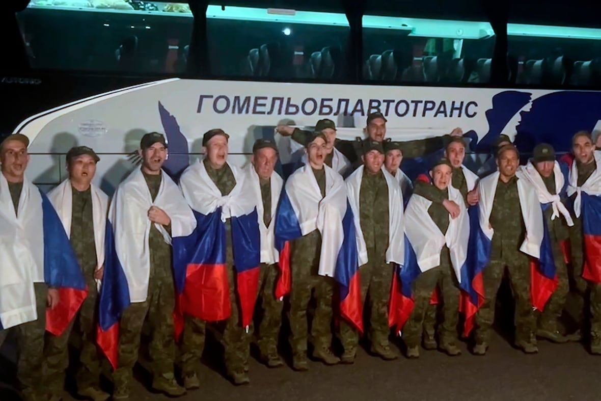 Line of individuals dressed in army camoflage, each with a Russian flag wrapped around them.