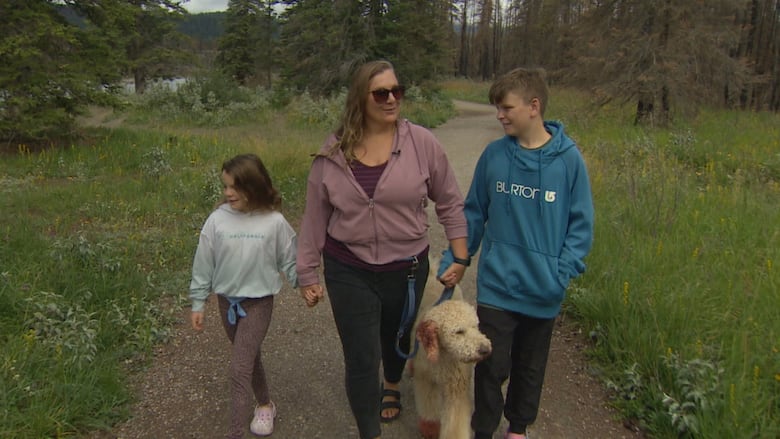 A woman walks in between two young children outside in a national park.