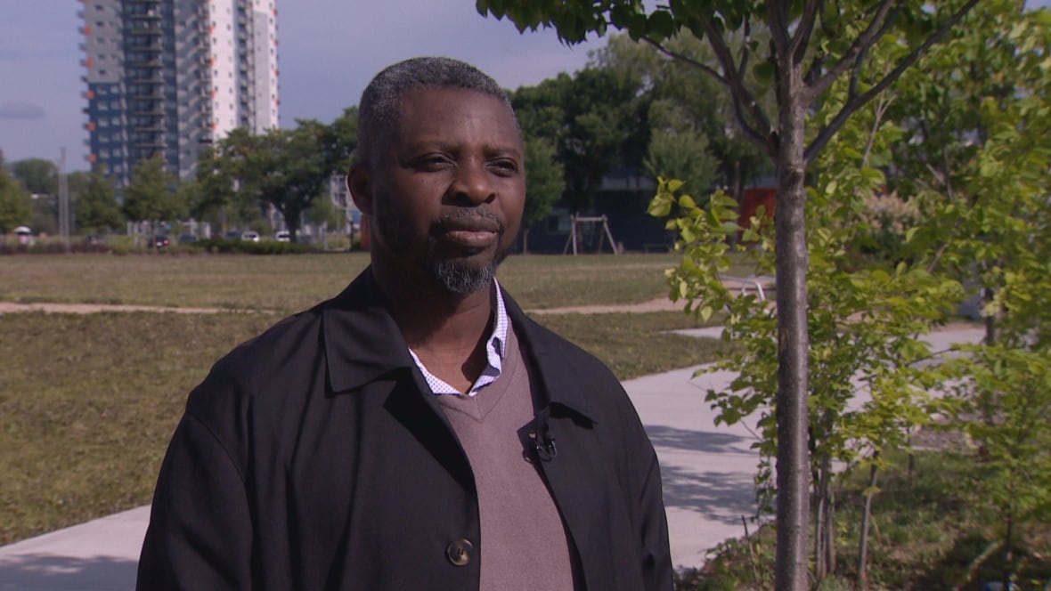 A man wearing a black jacket stands in a park.